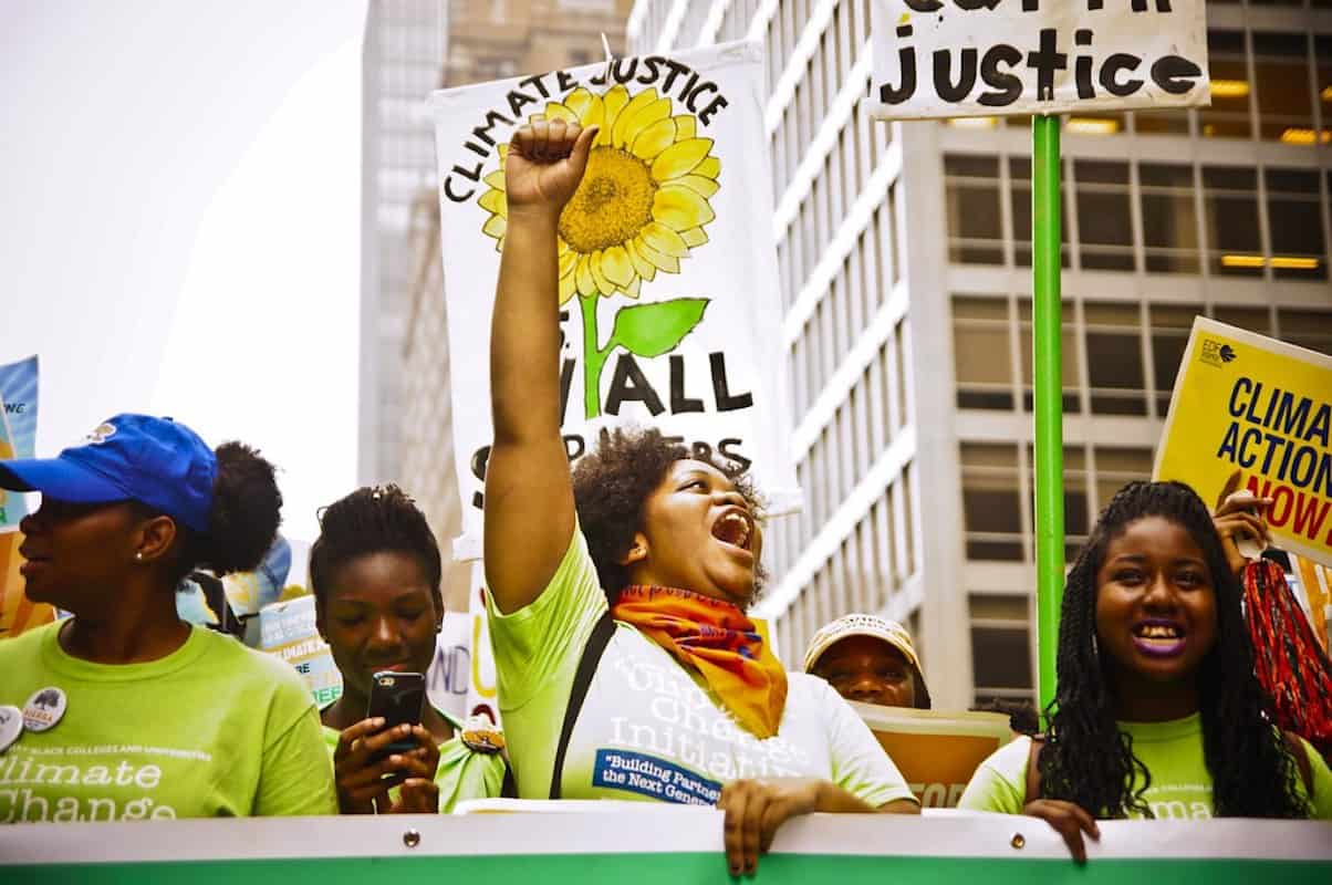 Climate activists holding a demonstration holding placards. One placard reads "Climate Justice for All"