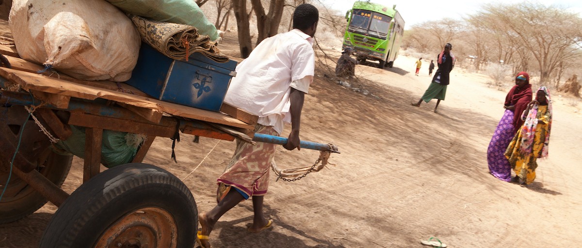 A man pulling a cart on a dusty street.
