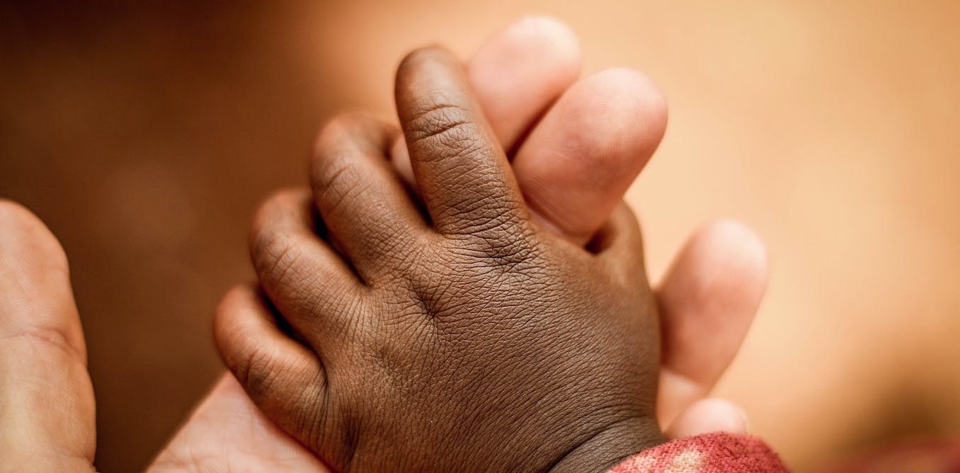 African baby holding a parent's two fingers